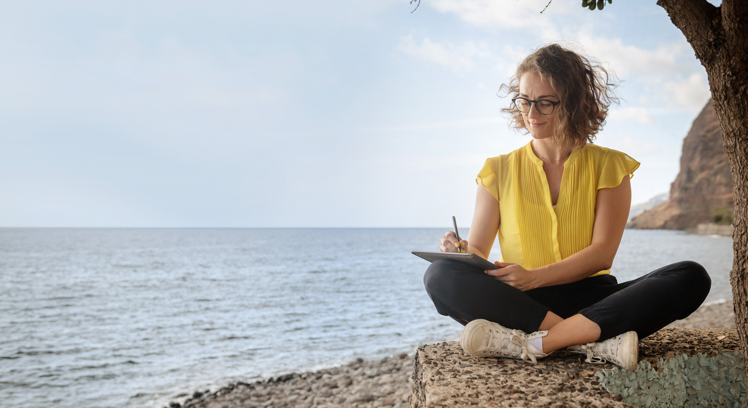 Symbolbild Workation buchen: Frau arbeitet bei Workation auf Madeira mit Tablet am Meer